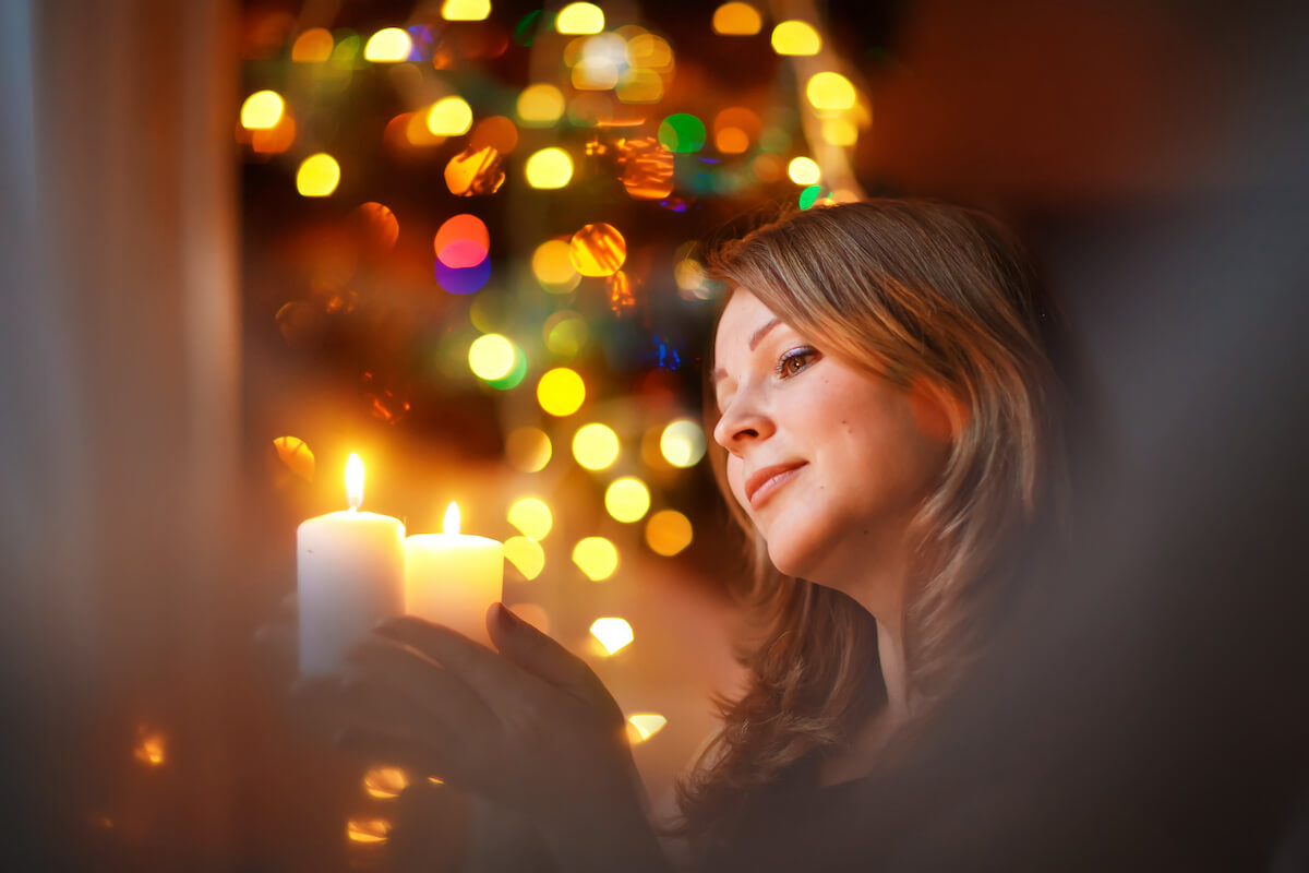 Woman in front of christmas tree lighting a holiday candle in honor of loved one_dealing with grief during the holidays