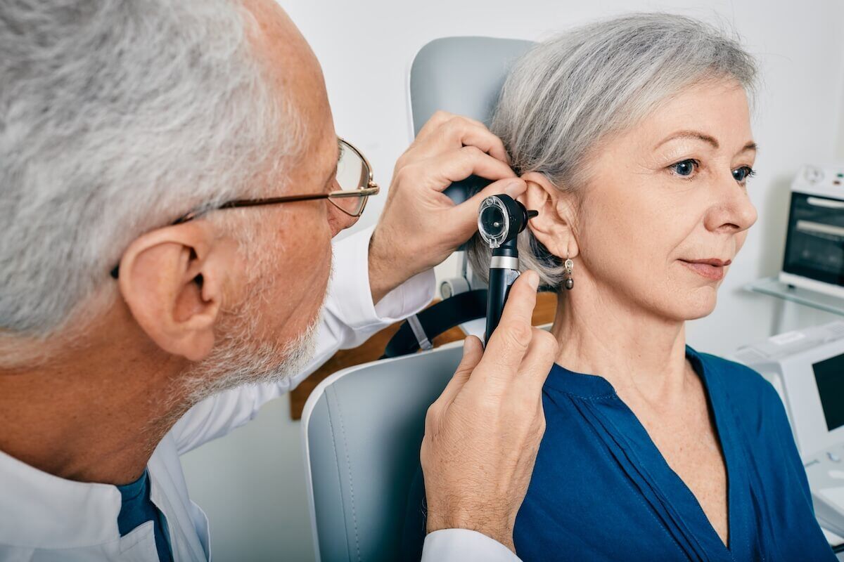 Otolaryngologist doctor checking senior woman's ear using otoscope